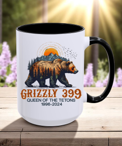 White 15oz ceramic coffee mug with a black handle and black on the inside of the cup that has a drawing of Grizzly 399 with the Teton Mountains in the background and under the bear the wording states Grizzly 399 Queen of the Tetons 1996-2024.