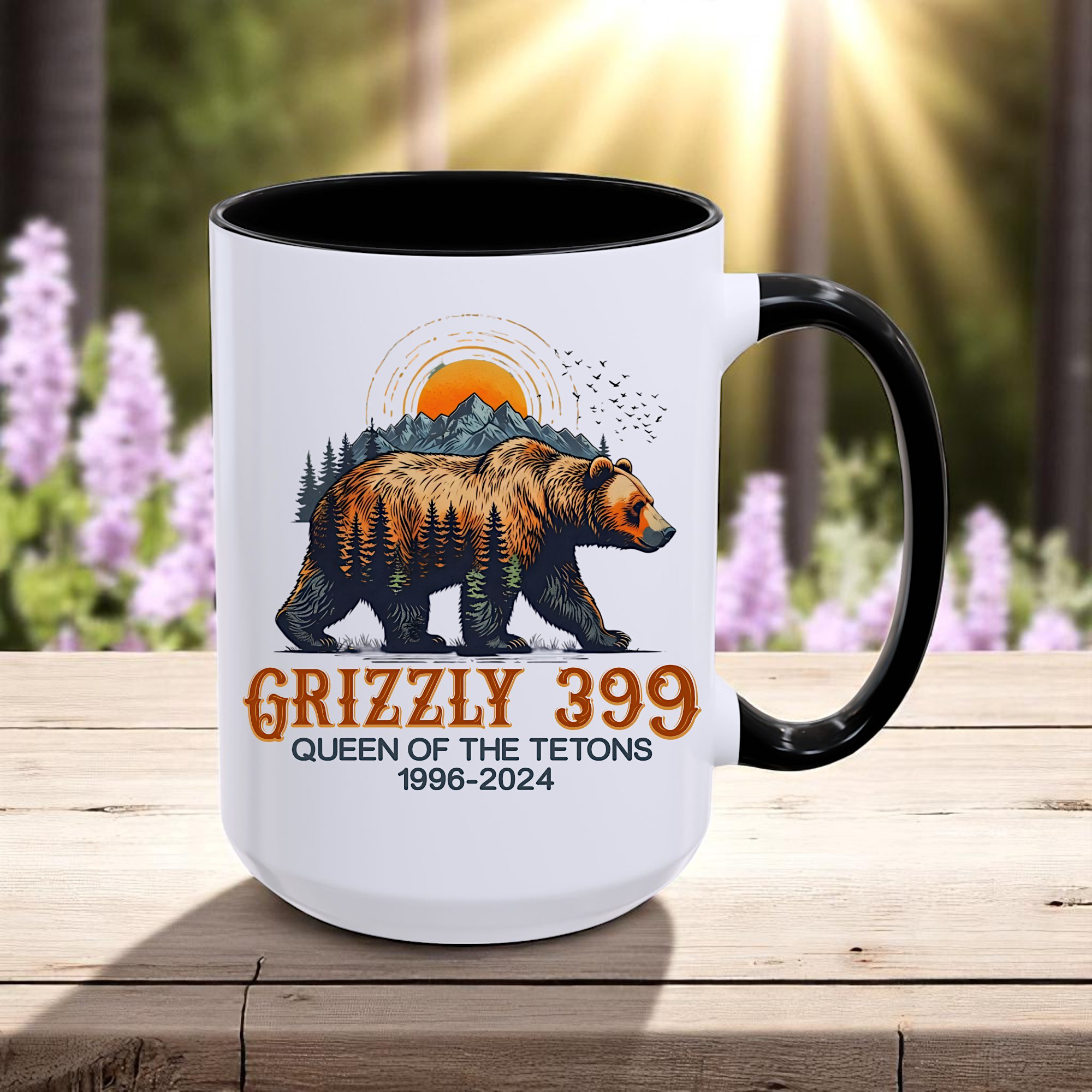 White 15oz ceramic coffee mug with a black handle and black on the inside of the cup that has a drawing of Grizzly 399 with the Teton Mountains in the background and under the bear the wording states Grizzly 399 Queen of the Tetons 1996-2024.